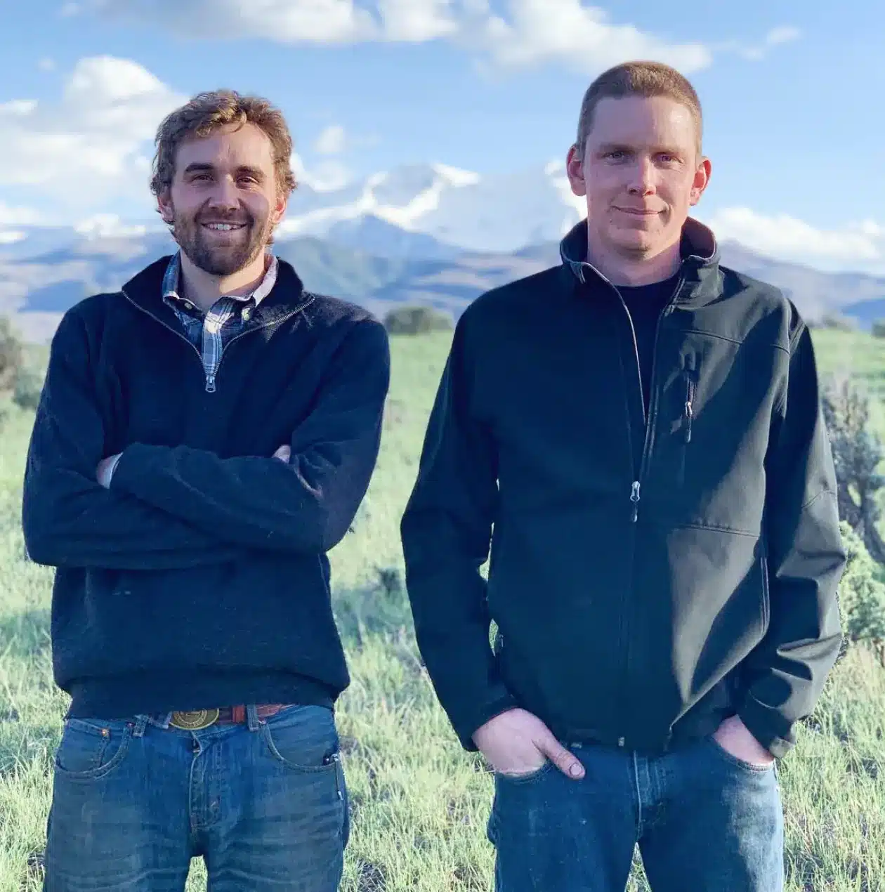 two men standing in a field with mountains in the background