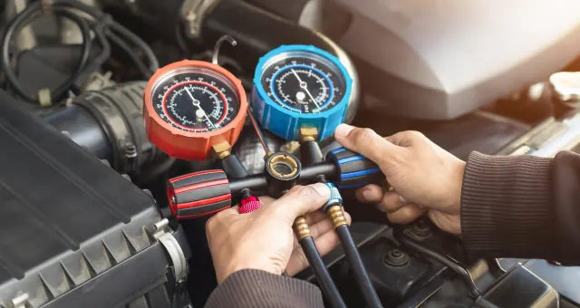 hands holding a gauge and a couple of hoses
